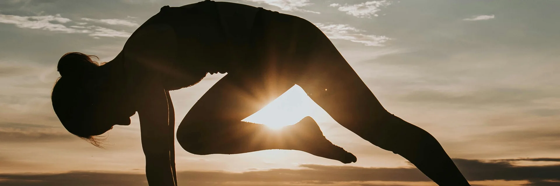Silhouette einer Frau in Yoga-Pose am Strand bei Sonnenuntergang