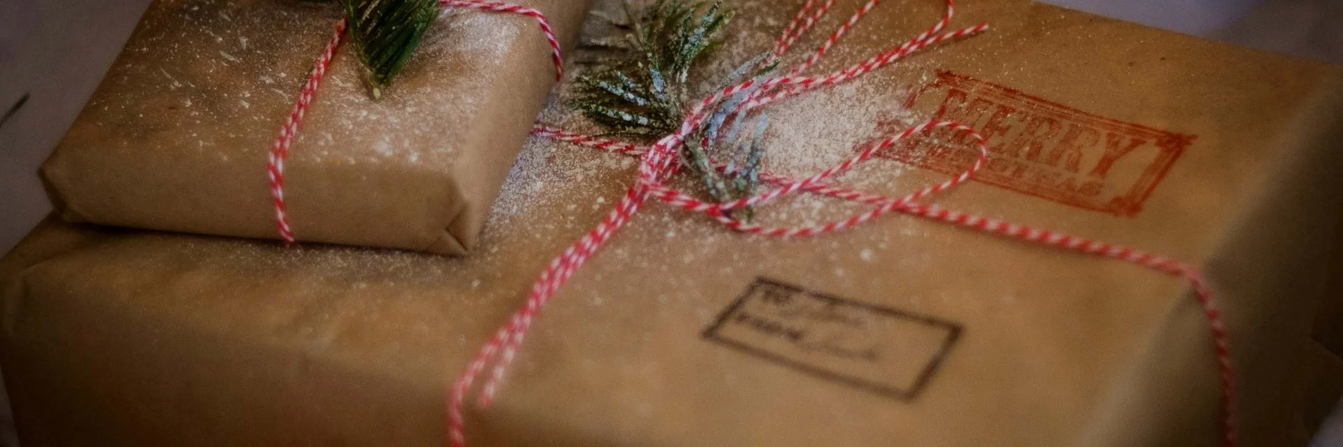 Zwei Geschenkpakete in braunem Papier mit rotem Band und Tannenzweigen dekoriert