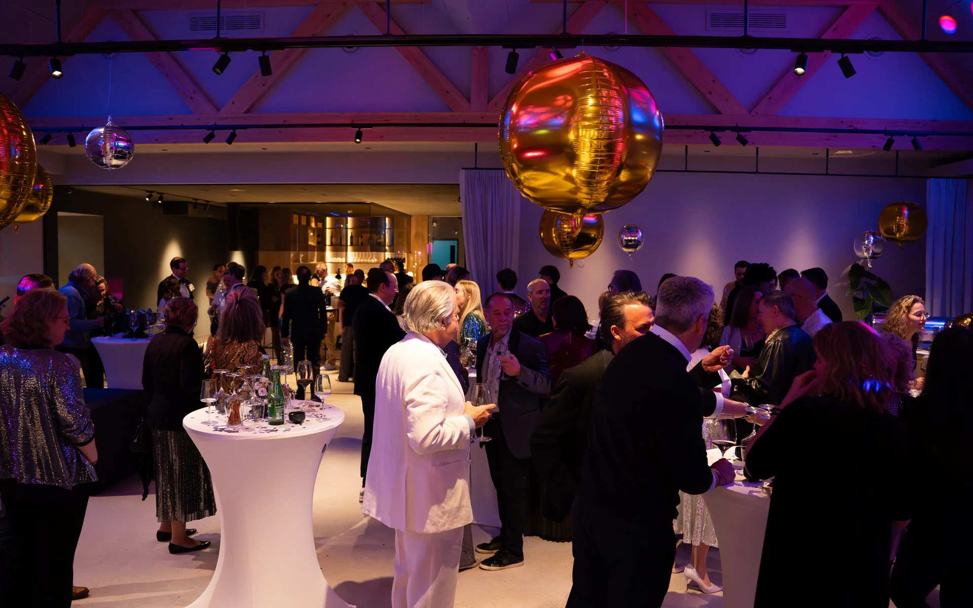 Menschen bei einer Feier mit Stehtischen und bunten Lichtern in einem Saal