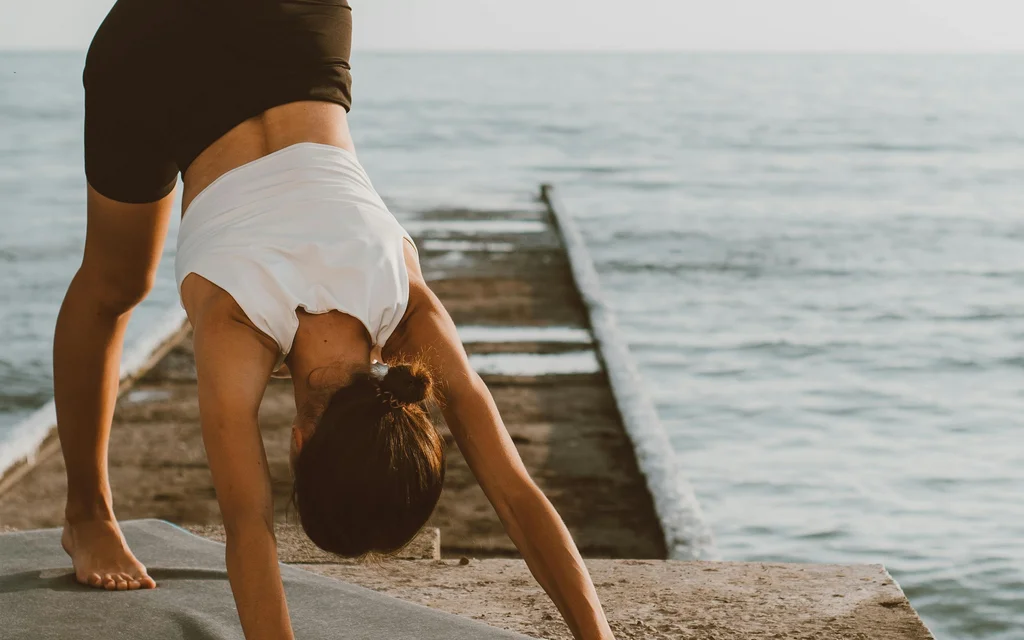 Frau macht Yoga mit einem Bein auf einem Steg am Meer