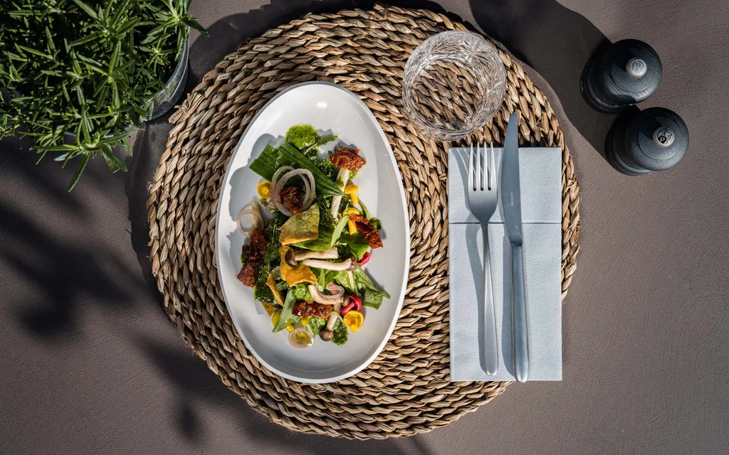 Salat auf weißem Teller mit Glas, Besteck und Gewürzmühlen auf Tisch