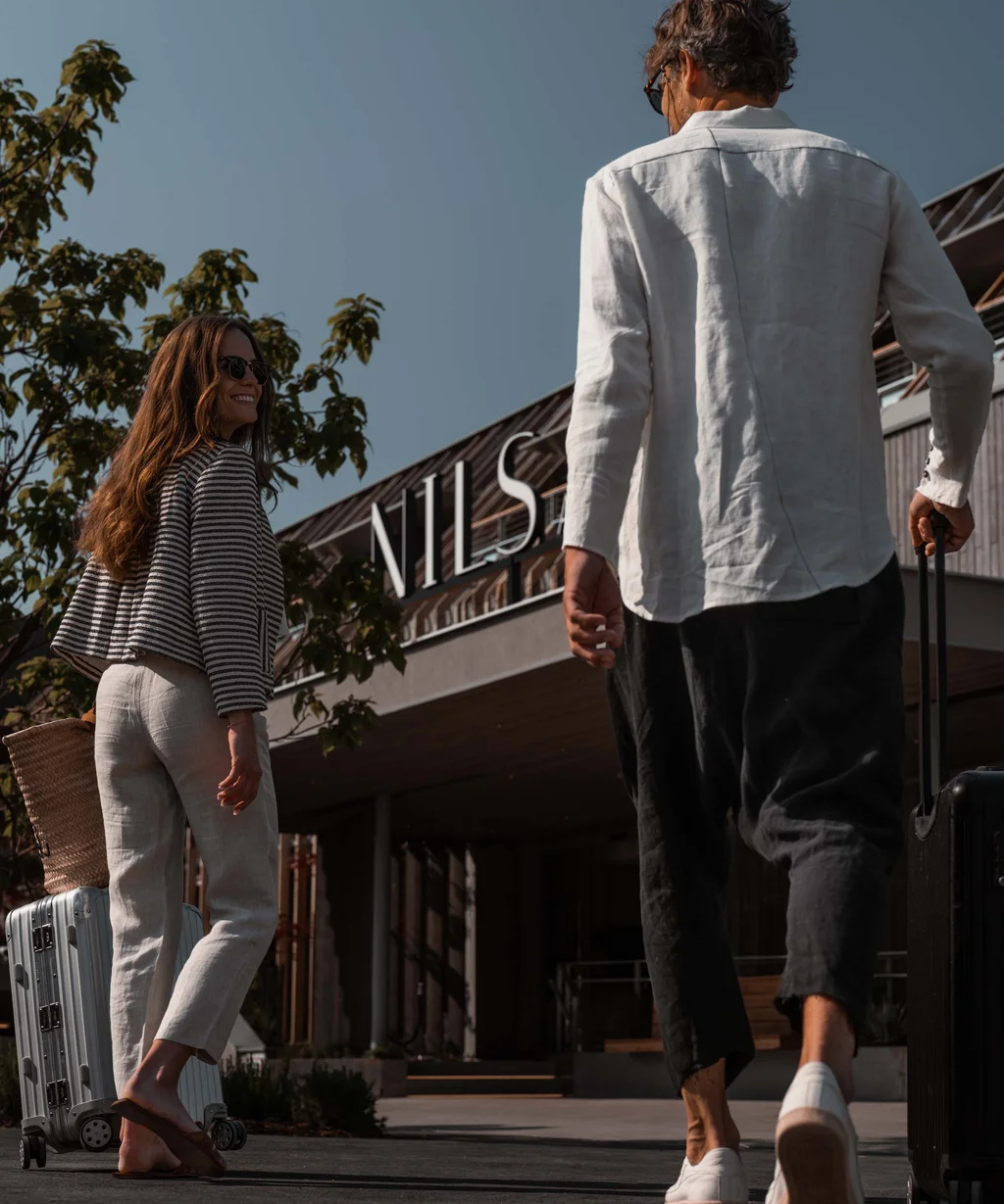 NILS am See: das Boutiquehotel am Neusiedler See Paar mit Koffern läuft zum Gebäude mit Schild NILS