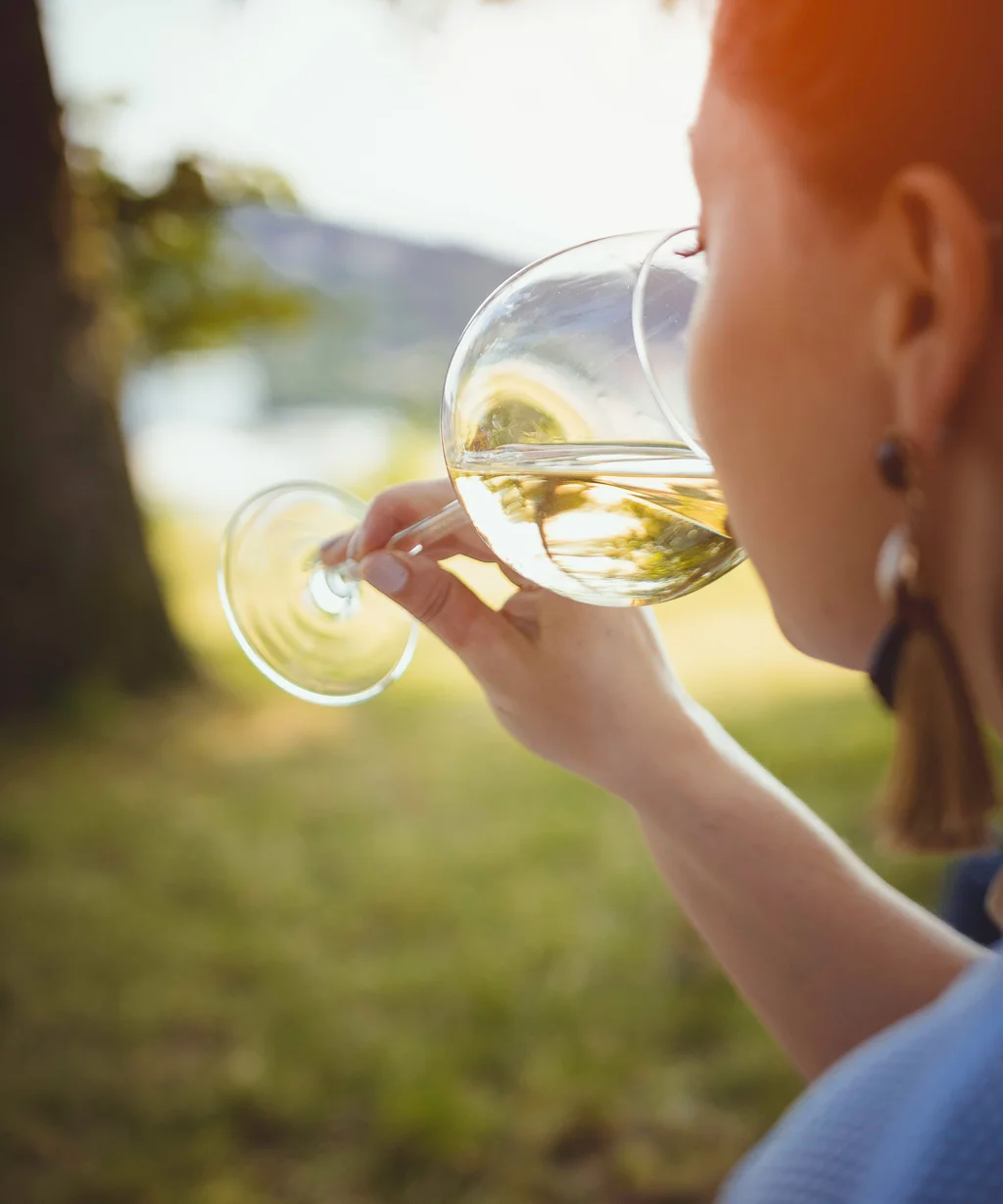 The NILS am See near Parndorf: your hotel at Lake Neusiedl Woman drinking white wine outdoors in sunlight among trees