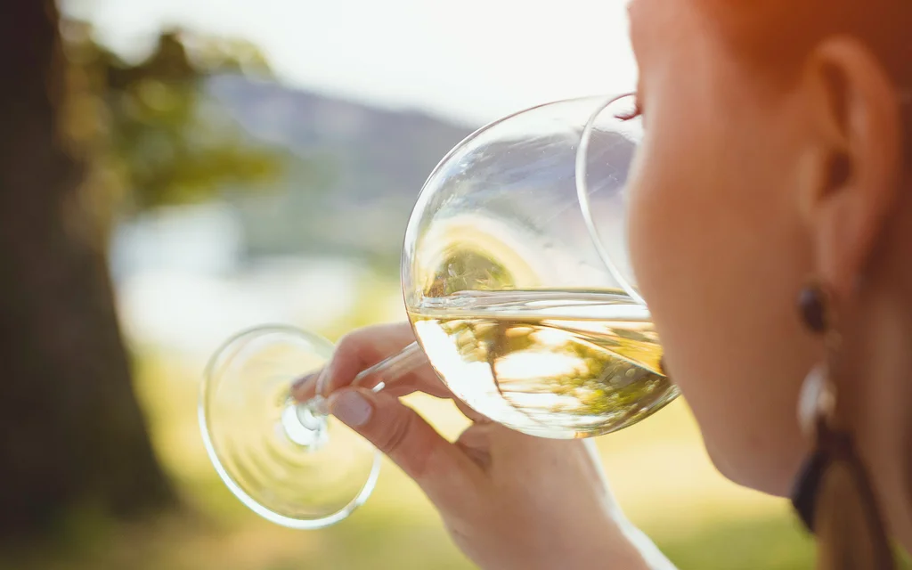 Frau trinkt Weißwein draußen bei Sonnenlicht zwischen Bäumen