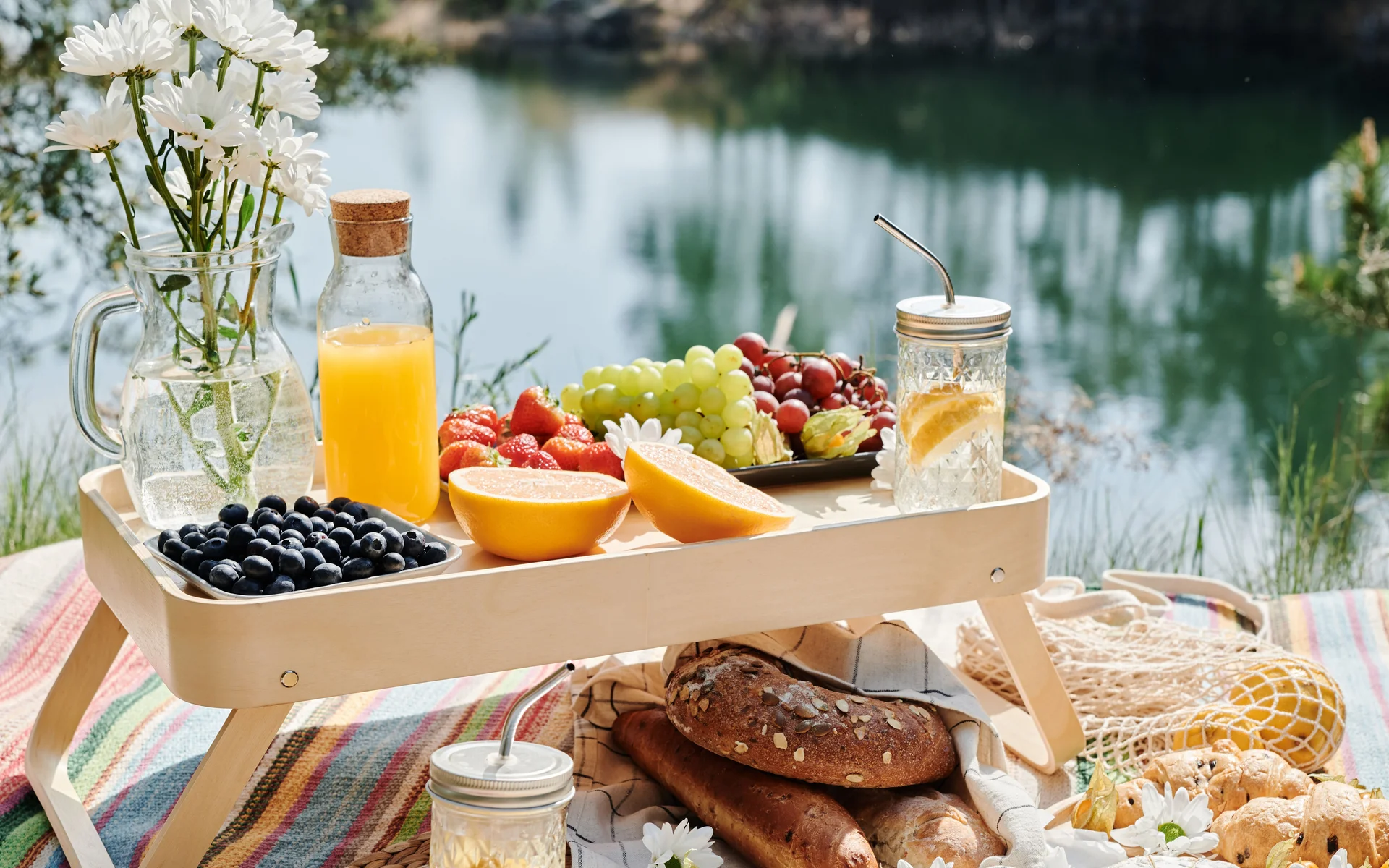 News aus dem NILS am See Picknick mit Obst, Brot, Getränken und Blumen auf Decke am See
