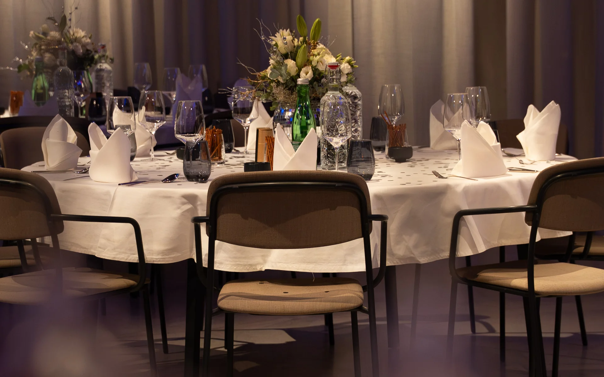 Eleganter gedeckter Tisch mit Blumenarrangement und Weingläsern in gedämpftem Licht