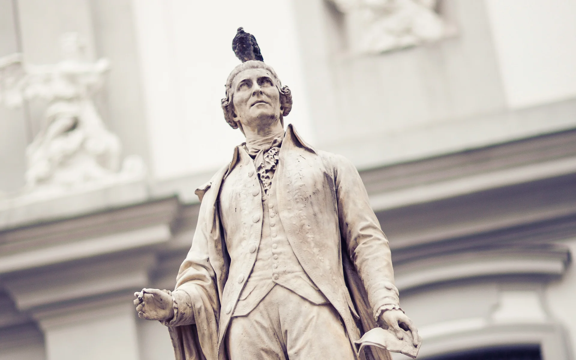 Steinerne Statue eines Mannes mit Tauben auf Kopf und Sockel