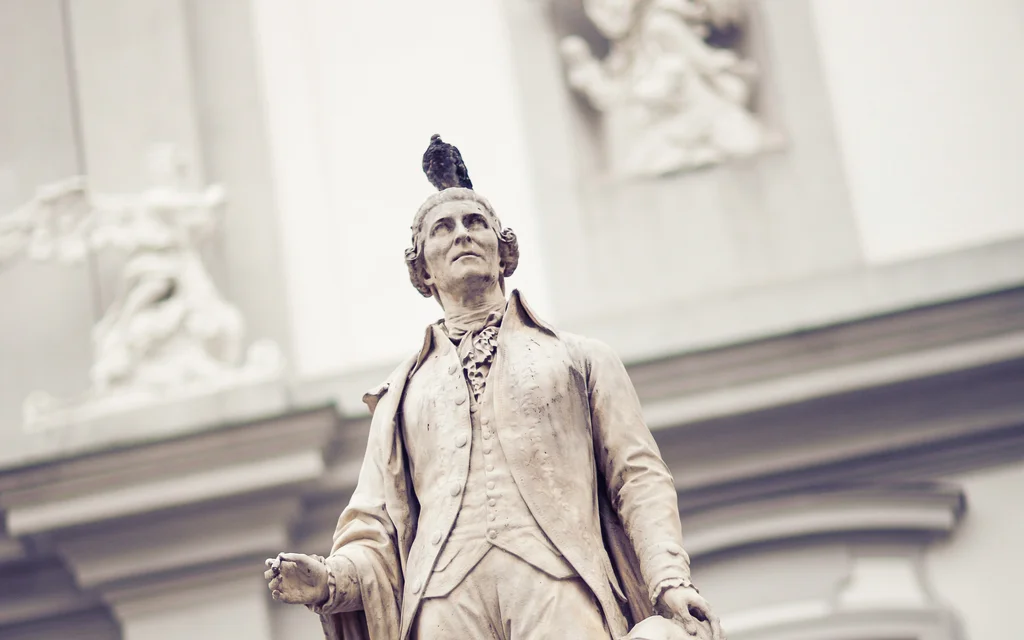 Steinerne Statue eines Mannes mit Tauben auf Kopf und Sockel