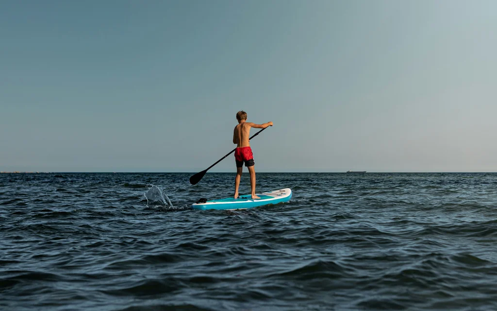 Junge beim Stand-up-Paddeln auf dem offenen Meer unter klarem Himmel