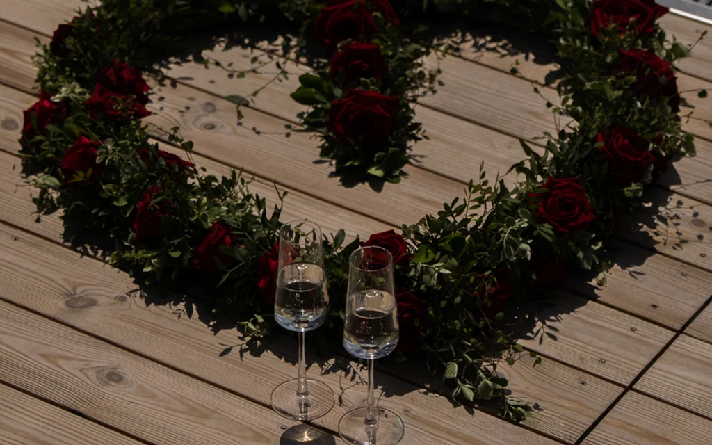Herz aus roten Rosen mit zwei gefüllten Champagnergläsern auf Holzboden