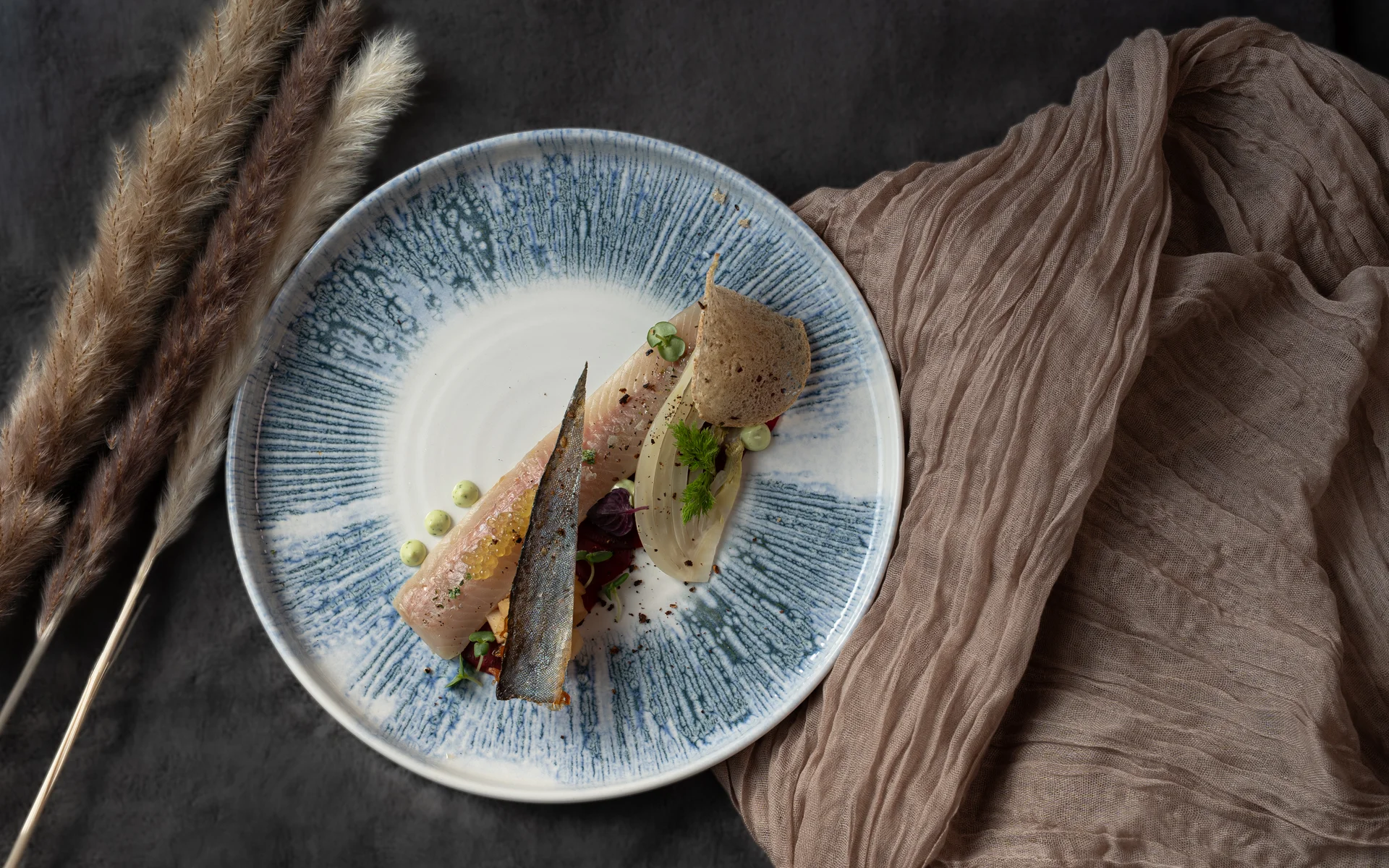 Fein angerichteter Fisch mit Beilagen auf graublaue Keramikplatte