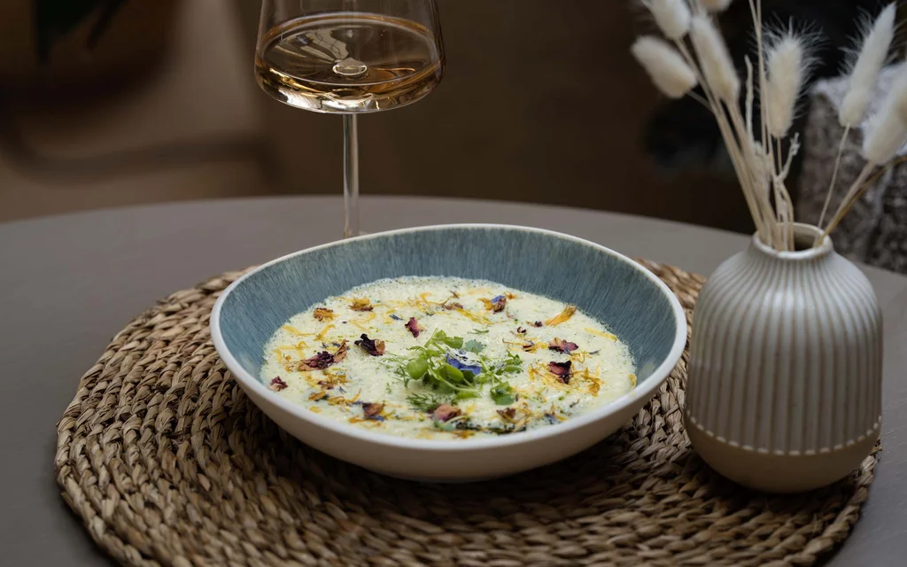 Suppenschüssel mit cremiger Suppe und essbaren Blüten auf einem gewebten Platzset